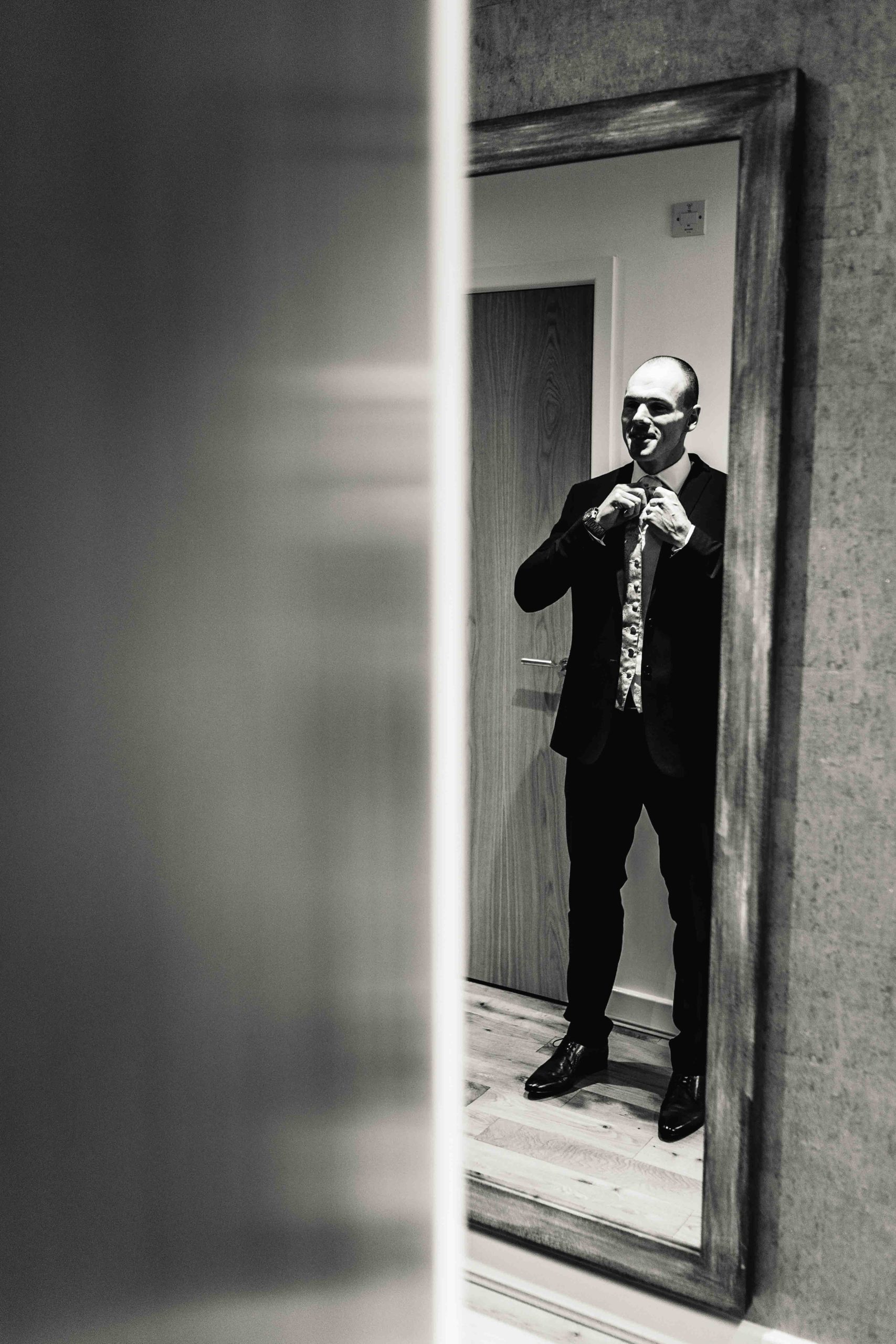 Groom stood in mirror getting ready before wedding